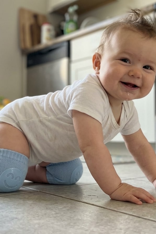 Smiling baby on all fours on the kitchen tiles, wearing their knee pads