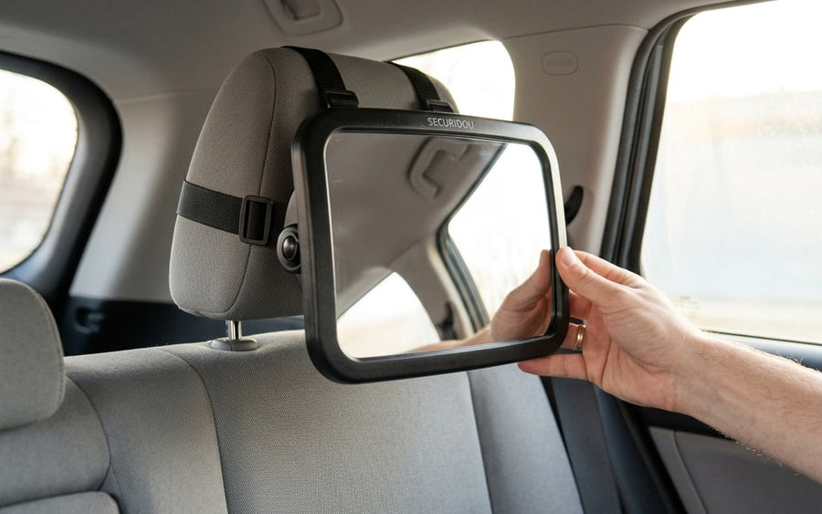 Hand angling the mirror on its ball joint, fitted to the rear headrest