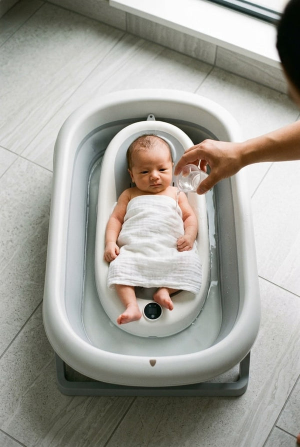 Newborn on the reclining cushion of the foldable bath, a muslin cloth over their tummy